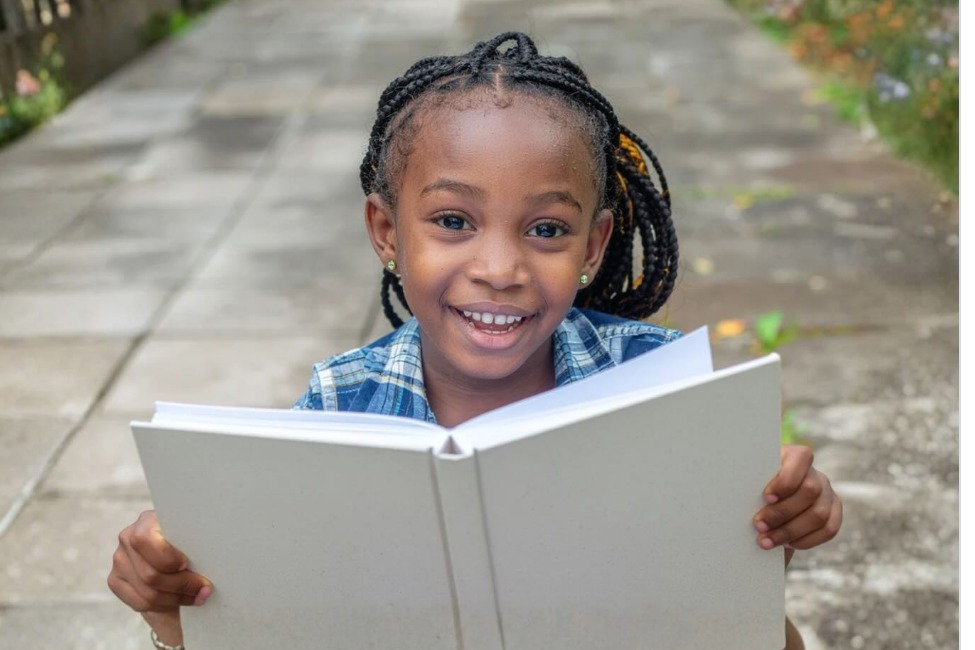 Criança sorrindo segurando um livro aberto, foto real do acompanhamento da clínica